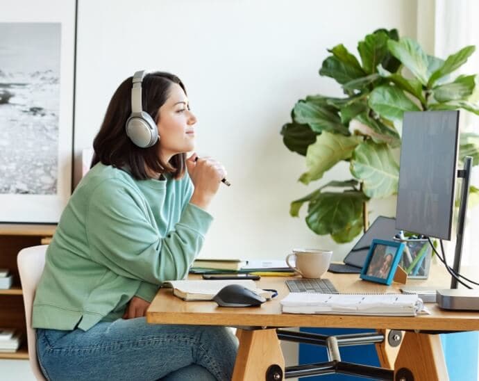 Mujer con auriculares sosteniendo un bolígrafo y mirando un monitor