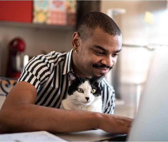 Hombre utilizando una computadora portátil mientras sostiene un gato