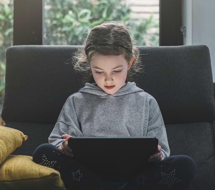 Chica en un sofá utilizando una computadora portátil e iniciando Norton Family.